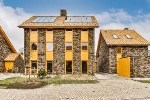 Conjunto de viviendas adosadas de construcción industrializada con ladrillo oscuro, ventanas verticales enmarcadas en madera y paneles solares integrados en el tejado, ejemplificando el futuro de los hogares eficientes.