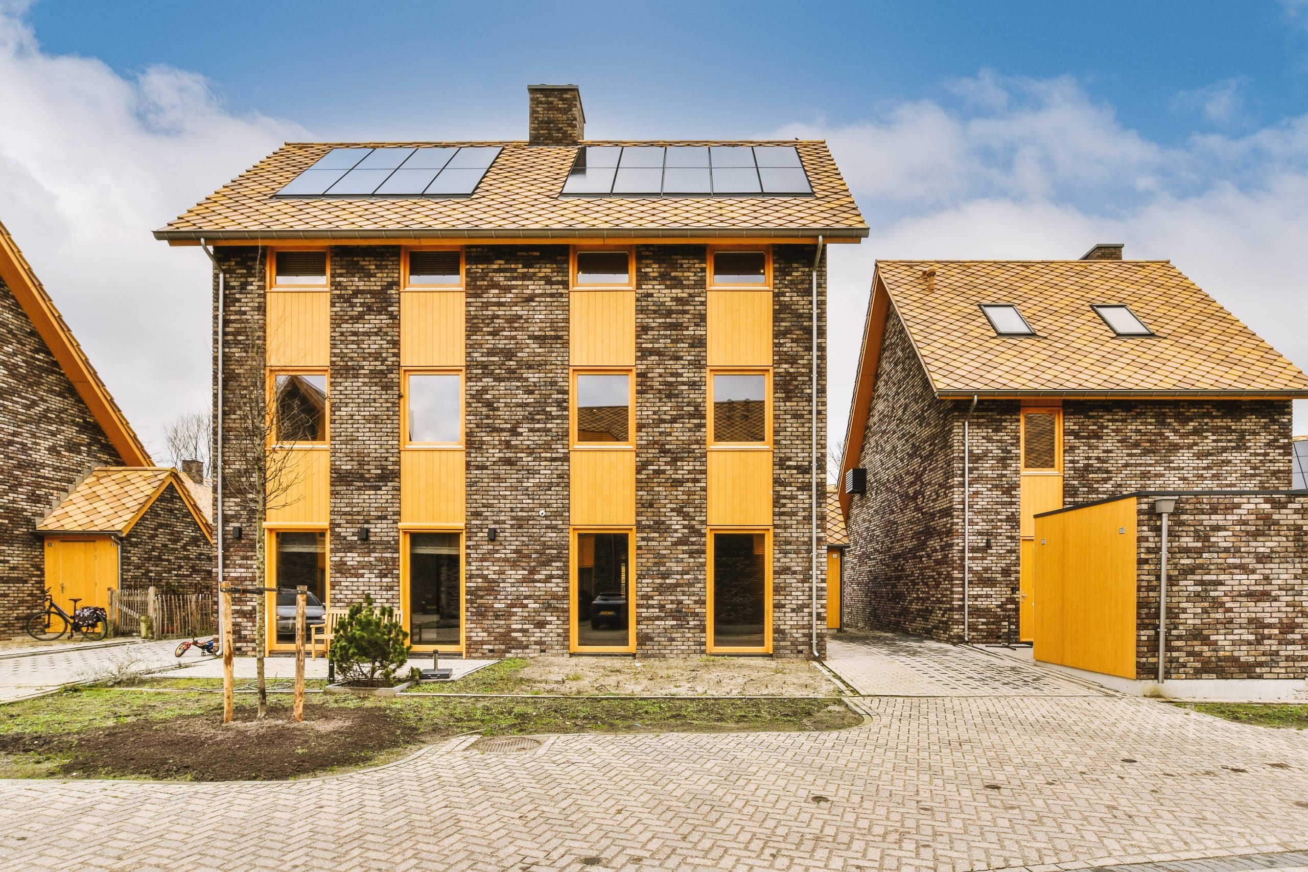 Conjunto de viviendas adosadas de construcción industrializada con ladrillo oscuro, ventanas verticales enmarcadas en madera y paneles solares integrados en el tejado, ejemplificando el futuro de los hogares eficientes.