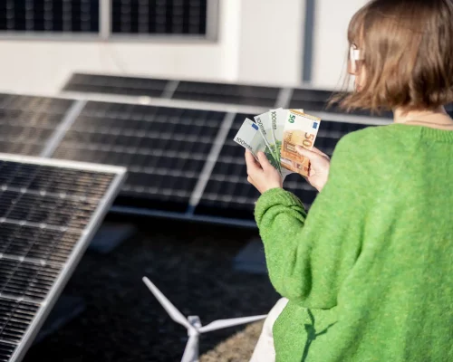 Mujer contando billetes de euro con una instalación de placas solares y una mini turbina eólica de fondo, simbolizando el ahorro energético