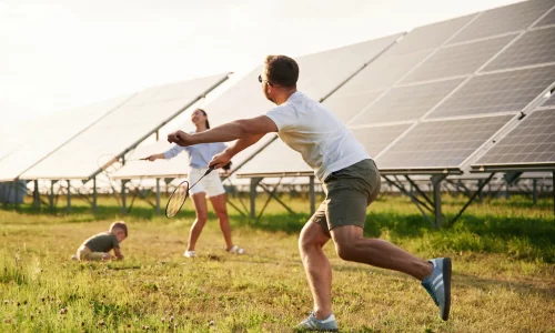 Familia jugando al bádminton al aire libre junto a una instalación de paneles solares fotovoltaicos, simbolizando un futuro sostenible